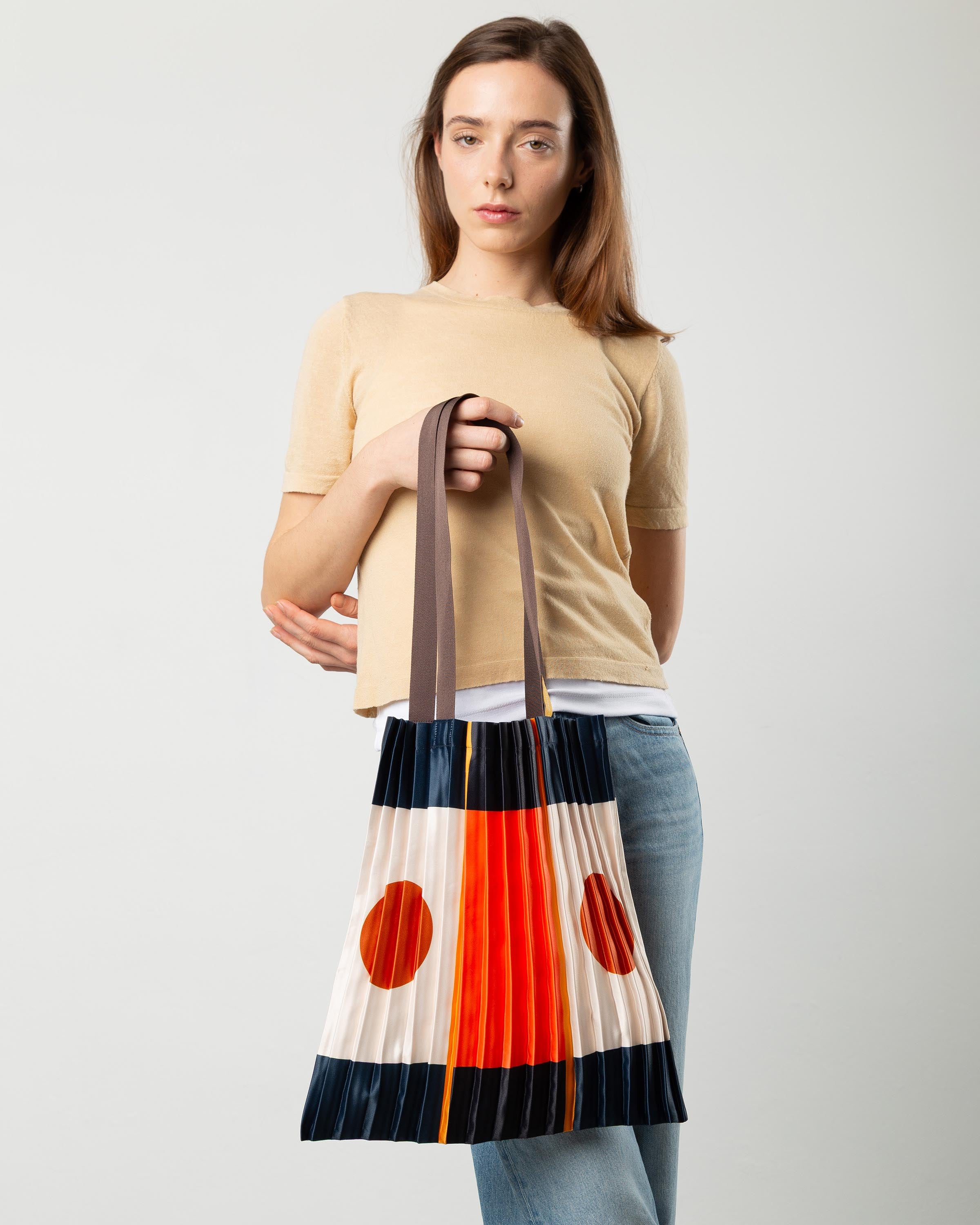 Tote bag plissettata di Multitudes indossata. Colore blu, bianco e arancione.